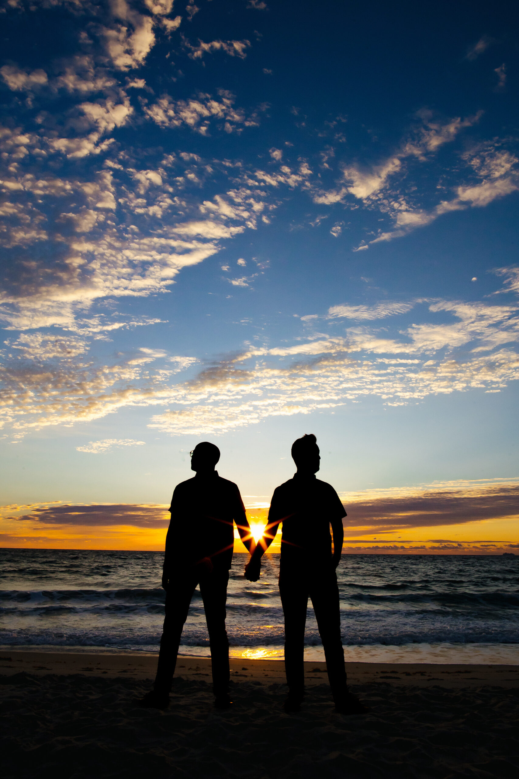 A Silhouette of two men holding hands in front of blue skies at Fort Lauderdale Beach