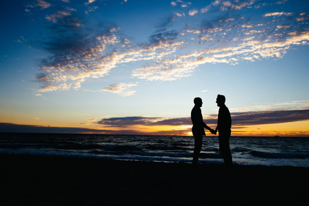Two fiancés holding hands in front of the ocean and gorgeous Blue Skies at Sunrise in Fort Lauderdale, Florida