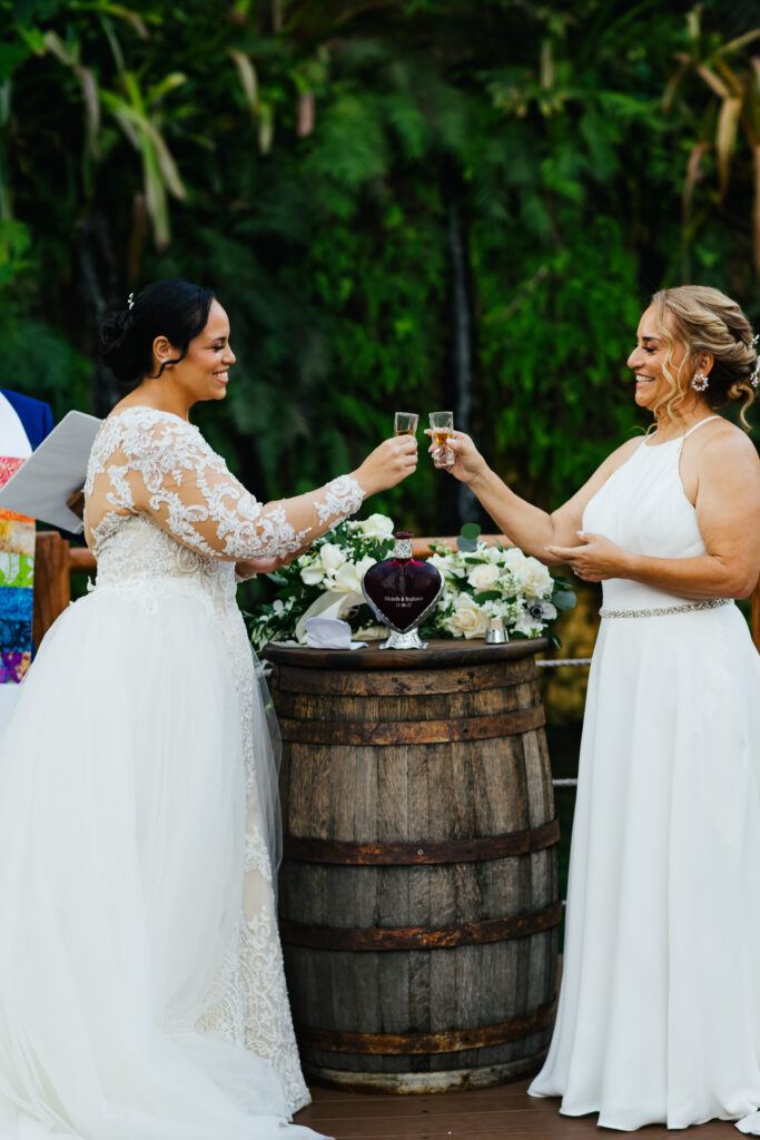 Two Brides dressed in white gowns celebrating their Wedding with a Tequila shot.