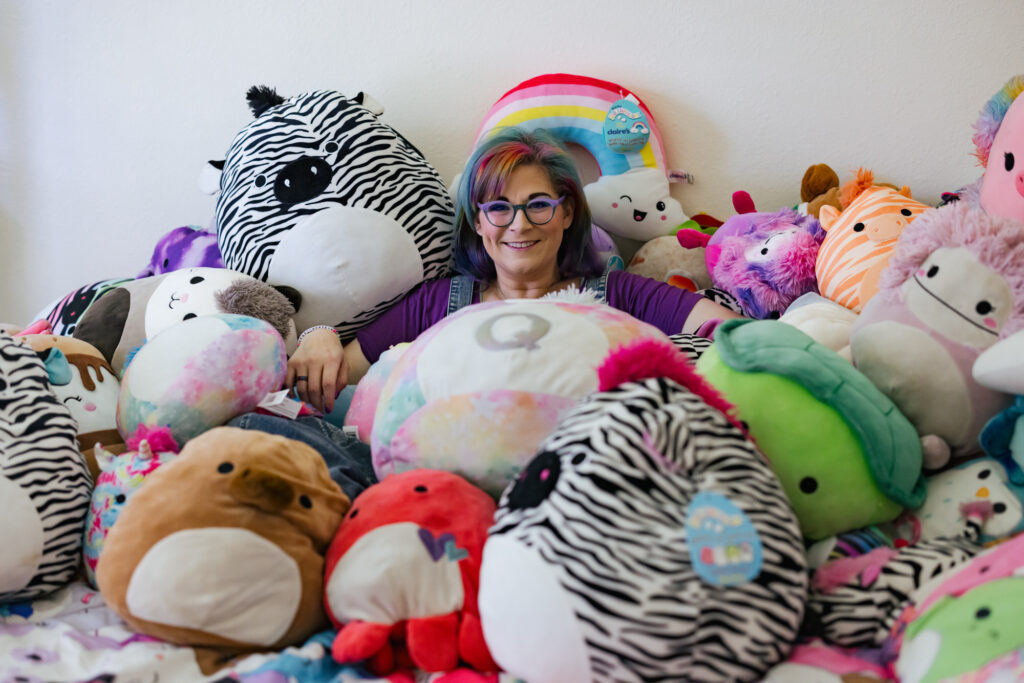 Colorful Art Teacher posing under her collection of Squishmallow plushies