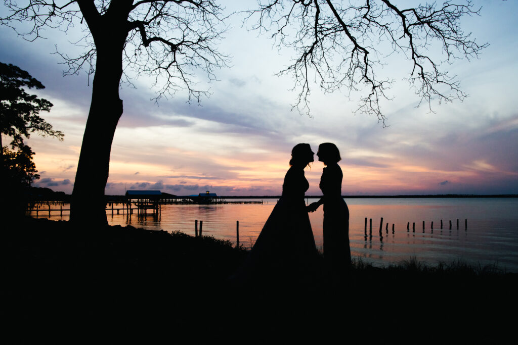 Silhouette at sunset with cotton candy sky of two Brides kissing