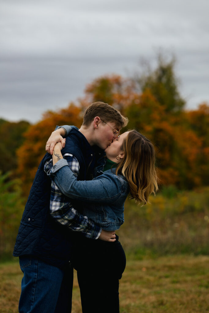 Engaged couple kissing with fall foliage in the distance